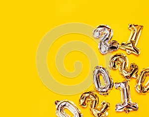 Gold and silver foil number balloons pattern on a yellow background