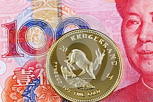 A gold South African krugerrand with a red 100 Chinese yuan bank note close up