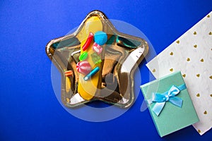 Gold star-shaped plate with eclair, gift box, napkin on bright blue table flatly