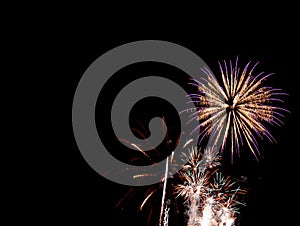 Gold starburst with purple edged firework above several small gold and green bursts with a black background