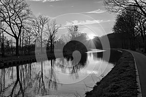 Gold sunset over river with sun rays, tree silhouettes and reflection on water in black and white