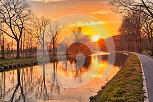 Gold sunset over river with sun rays, tree silhouettes and reflection on water