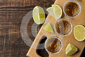 Gold tequila in a glass shot glass with salt and lime on a brown wooden background. top view with space for text