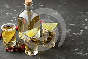 Gold tequila in a glass shot glass with salt, lime and hot pepper on a black concrete background. bar. alcoholic beverages