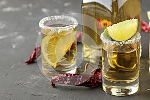 Gold tequila in a glass shot glass with salt, lime and hot pepper on a black concrete background. bar. alcoholic beverages