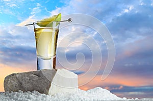 Gold tequila in a glass with slice of lime on a skewer stands on a stone against a beautiful sunset in the desert