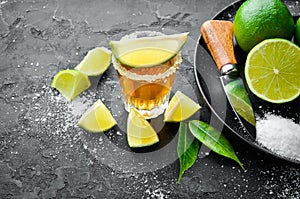 Gold tequila with lime and salt on black stone background. Top view.