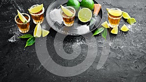 Gold tequila with lime and salt on black stone background. Top view.