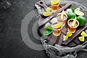 Gold tequila with lime and salt on black stone background. Top view.