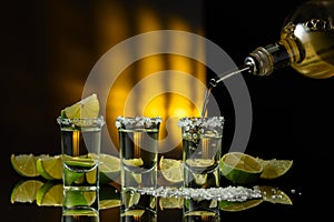 Gold tequila with sea salt and lime slices on a black reflective background