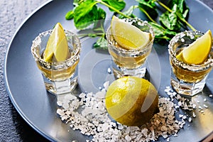 Gold tequila shot with lime and sea salt on grey plate