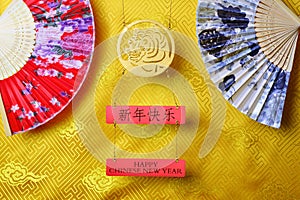 Gold tiger symbol and pair of chinese bamboo paper fans on yellow fabric with traditional chinese ornament with clouds. Chinese