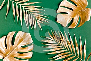 Gold tropical palm leaves Monstera on green background. Flat lay, top view minimal concept.