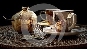 a gold vase sitting next to two coffee cups on a plate