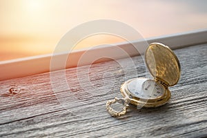 Gold Vintage pocket watch with sunset light on wooden background. Hourglass or sand timer, symbol of time. Selective focus