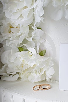 Gold wedding rings on a background of white decorative flowers. Vertical photography