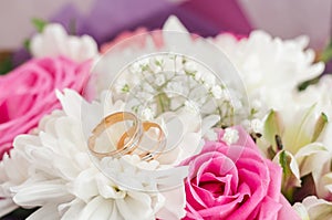 Gold wedding rings on a bouquet of white and pink flowers