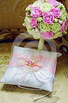 Gold wedding rings on a decorative satin cushion with ribbons. The bride`s bouquet