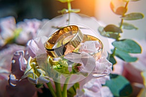 Gold wedding rings and delicate pink flowers, selective focus, close-up. Wedding photo with copy space