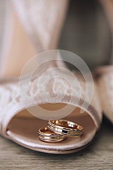 Gold wedding rings with a design are on the bride`s shoes with a lace. Close up