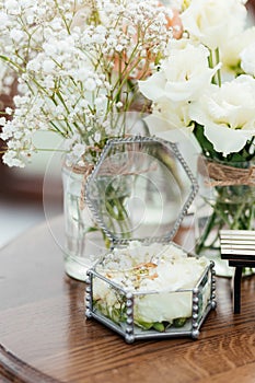 Gold wedding rings with diamonds in the box with roses at the background of the white flowers