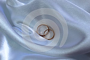 Gold wedding rings lie on satin fabric