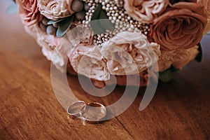 Gold wedding rings lie on a wooden table, against the background of the bride`s bouquet of roses. Wedding concept