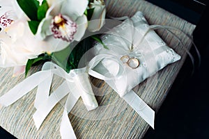 Gold wedding rings on a white cushion decorated with ribbons and flowers, close-up. Wedding theme, accessories for newlyweds