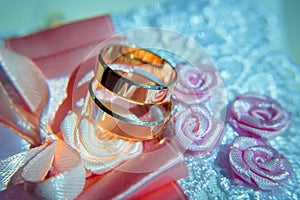 Gold wedding rings on a white cushion decorated with ribbons and flowers, close-up. Wedding theme, accessories for newlyweds