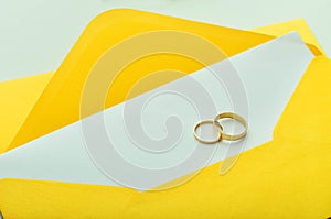 Gold wedding rings on the yellow letter invitation on the white background