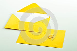 Gold wedding rings on the yellow letter invitation on the white background