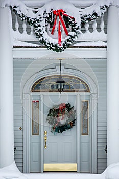 Gold and white front door decorated with Christmas decorations and snow