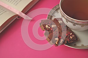 Gold and white porcelain tea cup and saucer with artisan chocolate on bright fuchsia pink background with copy space