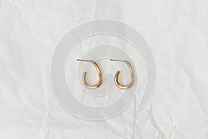 Gold women\'s earrings on a background of white crumpled paper close-up. Images for your design