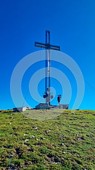 Goldeck - Man with baby carrier under massive summit cross of Goldeck, Latschur group, Gailtal Alps, Carintha, Austria