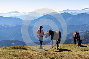 Goldeck - Woman holding baby and playing with herd of wild horses grazing on alpine meadow with scenic view of magical mountain