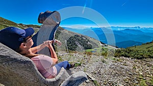 Goldeck - Woman relaxing on wooden chair with view of mountain peaks Karawanks and Julian Alps seen from Goldeck