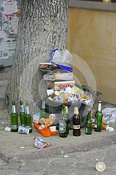 Golden age of consuming. Overflowing trash can on a street, empty bottles of alchohol, food boxes, plastic bags. Kyiv