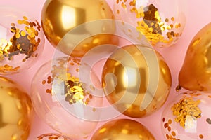 Golden air balloons with confetti inside on a pink background.