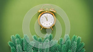 Golden alarm clock and decorative fir branch border on green paper background. Creative layout. Top view, flat lay. New