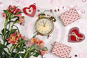 Golden alarm clock with gifts, alstroemeria flowers, hearts and confetti on light marble table