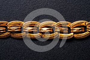 Golden antique jewelry chain on an isolated black background. Part of an old retro bracelet with links. Gold vintage
