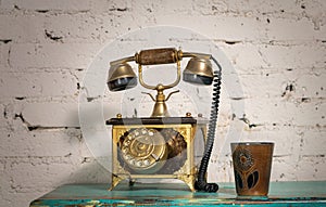 Golden antique telephone set and pottery mug on green vintage wooden table and white bricks wall