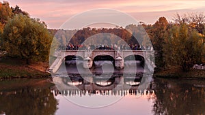 Golden autumn in Moscow parks. The dam of the Upper Tsaritsyno pond at sunset, people crossing the bridge.