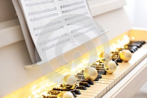 Golden baubles and fairy lights on piano keys, closeup. Christmas music