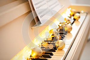 Golden baubles and fairy lights on piano keys, closeup. Christmas music