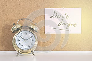 Golden bell alarm clock and a note writen DON`T FORGET on a cork board photo