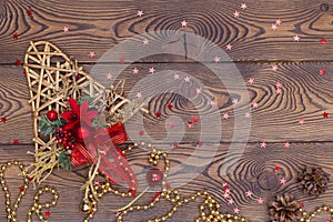 Golden bell from rattan with pine cones, Christmas toys, shiny beads and small red shiny stars on a wooden table. Top view, copy