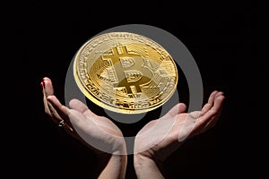 Golden bitcoin on black background over female hands. Cryptocurrency mining concept.