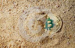 Golden Bitcoin coin buried in sand.